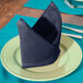 A plate with a folded navy blue Intedge cloth napkin on it.