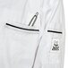 A white Chef Revival chef coat with black piping and a pen in the pocket on a kitchen counter.
