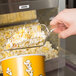 A hand using a Cal-Mil Classic plastic scoop to pour popcorn into a machine.