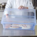 A chef wearing gloves holds a Carlisle blue plastic food storage box with food.