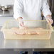 A chef in a white coat and gloves holding a Carlisle yellow food storage box filled with raw chicken.