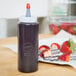 A Wilton squeeze bottle filled with strawberry sauce on a table next to a plate of strawberries.