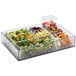 A clear acrylic square bowl filled with a variety of food.