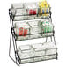 A black iron Cal-Mil three tier rack holding glass jars filled with condiments.