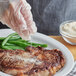 A gloved hand sprinkling Regal Onion Salt on a piece of meat with green beans.