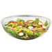 A clear acrylic salad bowl filled with salad and vegetables.