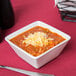 A Tuxton TuxTrendz bright white square china bowl filled with chili and cheese with a spoon.
