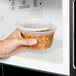A hand holding a Pactiv Deli Container of food in a microwave.