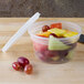 A Pactiv translucent plastic deli container with a lid filled with red grapes on a table.