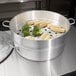 An aluminum steamer pot with corn and broccoli inside.