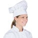 A woman wearing a white Chef Revival chef hat with an adjustable head band.