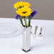 An American Metalcraft stainless steel bud vase with yellow flowers on a table.