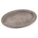 A Lodge oval wood underliner with a walnut finish under a round wooden plate on a table.