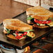 A Lodge cast iron griddle on a stovetop with two grilled sandwiches on it.
