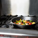 A Lodge cast iron skillet with vegetables cooking on the stove.
