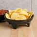 A black molcajete bowl filled with salsa and chips on a table.