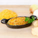 A Lodge mini cast iron oval casserole dish with food in it next to cheese and bread.