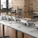 A buffet table with food in Choice Classic round chafers.