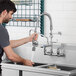 A man using a T&S pre-rinse faucet to wash dishes in a stainless steel sink.