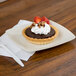 A Fineline ivory plastic dessert plate with a small chocolate tart topped with whipped cream and strawberries.