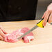 A person using a Mercer Millennia yellow narrow boning knife to cut meat on a cutting board.