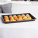 A black Cambro market tray holding croissants on a table.
