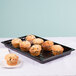 A black Cambro market tray with muffins on a white table.