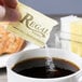 A hand holding a Regal Yellow Sucralose sugar substitute packet over a cup of coffee.