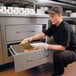 A woman using a Hatco drawer warmer on a counter in a professional kitchen to store food.