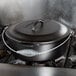 A black Lodge cast iron dutch oven with a spiral wire handle on a stove.