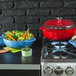 A Caribbean blue Lodge enameled cast iron Dutch oven on a stove top with a red pot and pan filled with vegetables.