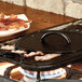 A Lodge cast iron flat grill press on a skillet with bacon cooking.