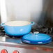A Lodge Caribbean blue enameled cast iron Dutch oven sits on a stove.