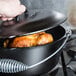 A hand using a Lodge cast iron Dutch oven to cook a chicken.
