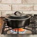 A Lodge pre-seasoned black cast iron pot with a lid on a gas stove.