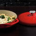 A Lodge Island Spice Red enameled cast iron casserole dish with food in it next to a red lid.