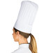 A woman wearing a white Chef Revival pleated flair style chef hat with a ponytail.