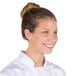 A brunette woman wearing a Chef Revival nylon hairnet and white chef's coat smiling in a professional kitchen.