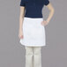 A woman wearing a Chef Revival white bistro apron with 2 pockets.