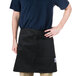 A man wearing a black Chef Revival bistro apron with 2 pockets standing in a professional kitchen.