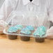 A person in gloves holding a Polar Pak plastic container with cupcakes.
