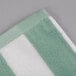 A close up of a mint green and white striped Oxford pool towel.