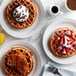 A plate with a waffle topped with strawberries, chocolate chips, and powdered sugar.