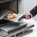 A person using an Amana PA10 oven paddle to cook a pizza in a professional kitchen oven.