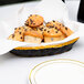 A Thunder Group black and gold rattan bread basket filled with muffins on a table.