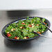 A bowl of salad with spinach, tomatoes, and croutons in a black Fineline oval bowl.