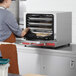 A woman putting cookies in an Avantco countertop convection oven.