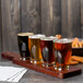 A mahogany flight paddle with Anchor Hocking Barbary tasting glasses filled with beer on a table in a brewery tasting room.