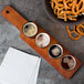A tray of Anchor Hocking Barbary Tasting Glasses on a mahogany flight paddle with beer and pretzels.