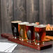 A wooden board with a row of four Anchor Hocking Barbary beer tasting glasses filled with beer.